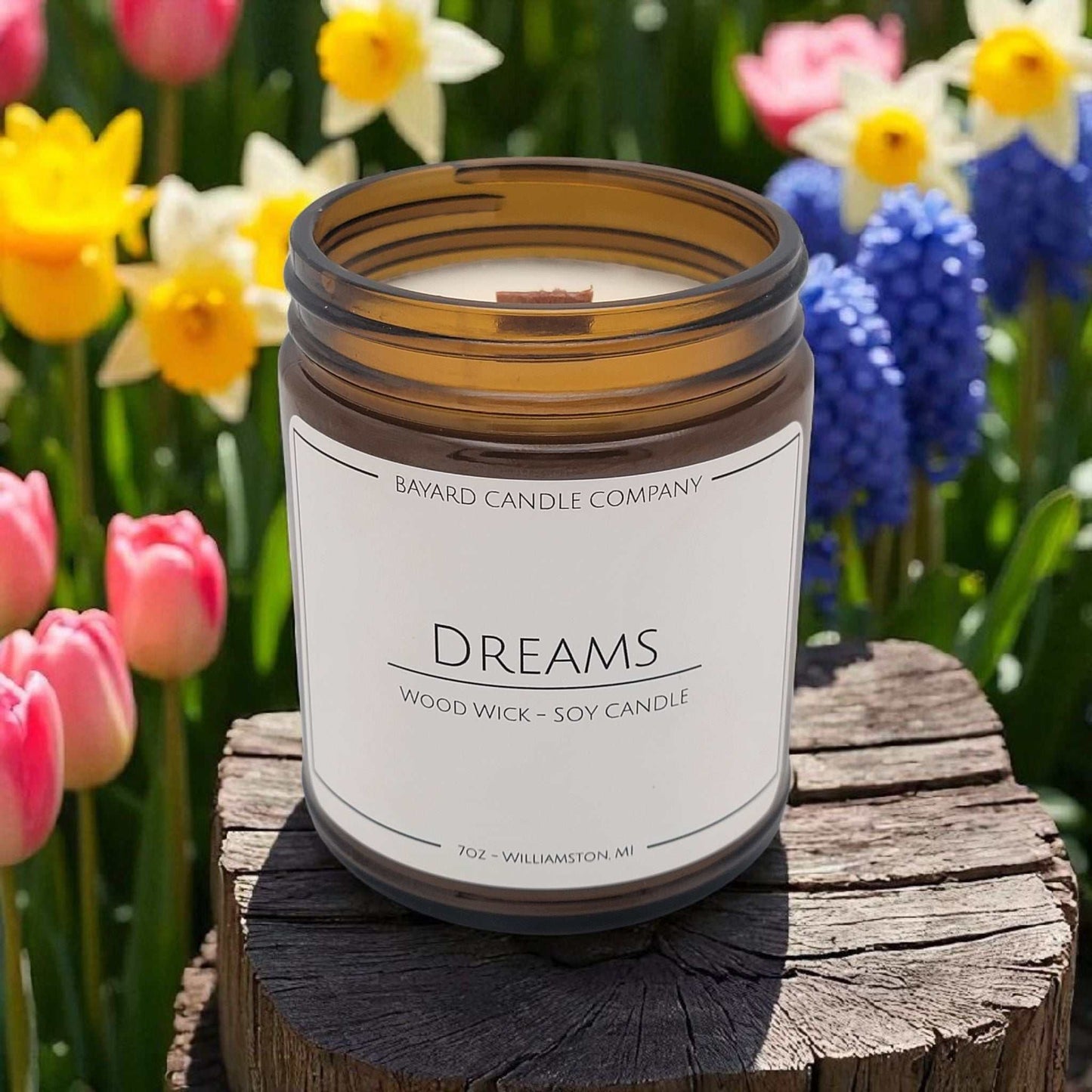 Dreams Wood Wick Candle on a stump by flowers