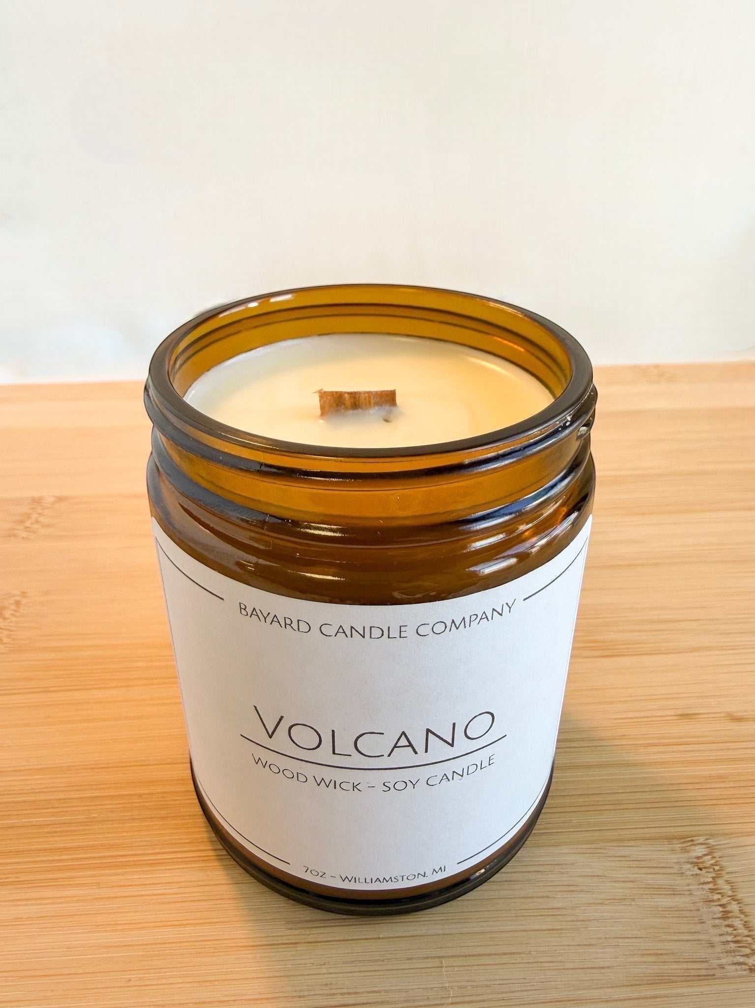 Volcano wood wick soy candle in amber glass jar without lid on showing woodwick wood surface, bright clean aesthetic