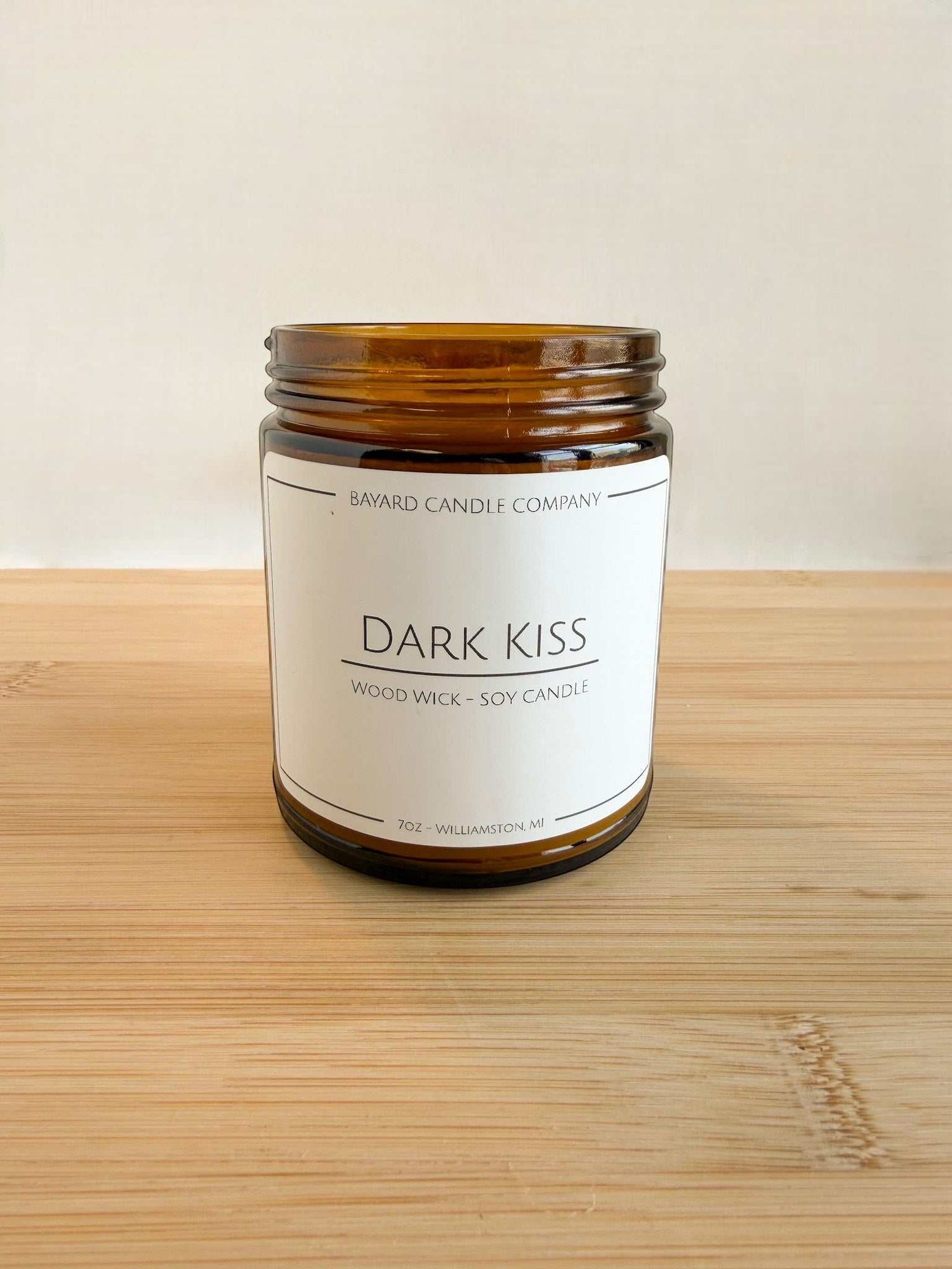 Dark Kiss soy candle in amber jar with clean label and minimalist background on wood surface