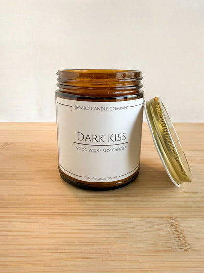 Dark Kiss wood wick soy candle with lid off in amber jar, showing candle detail and gold lid on wood surface