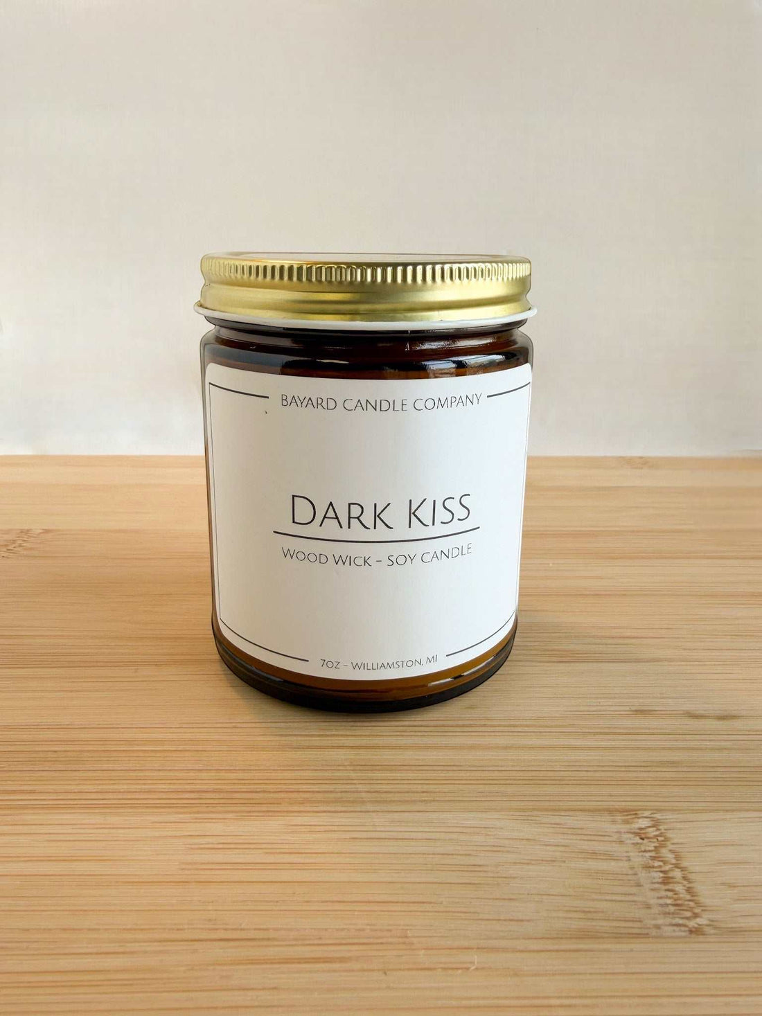 Dark Kiss wood wick soy candle in amber glass jar with gold lid on wood surface, clean minimalist background