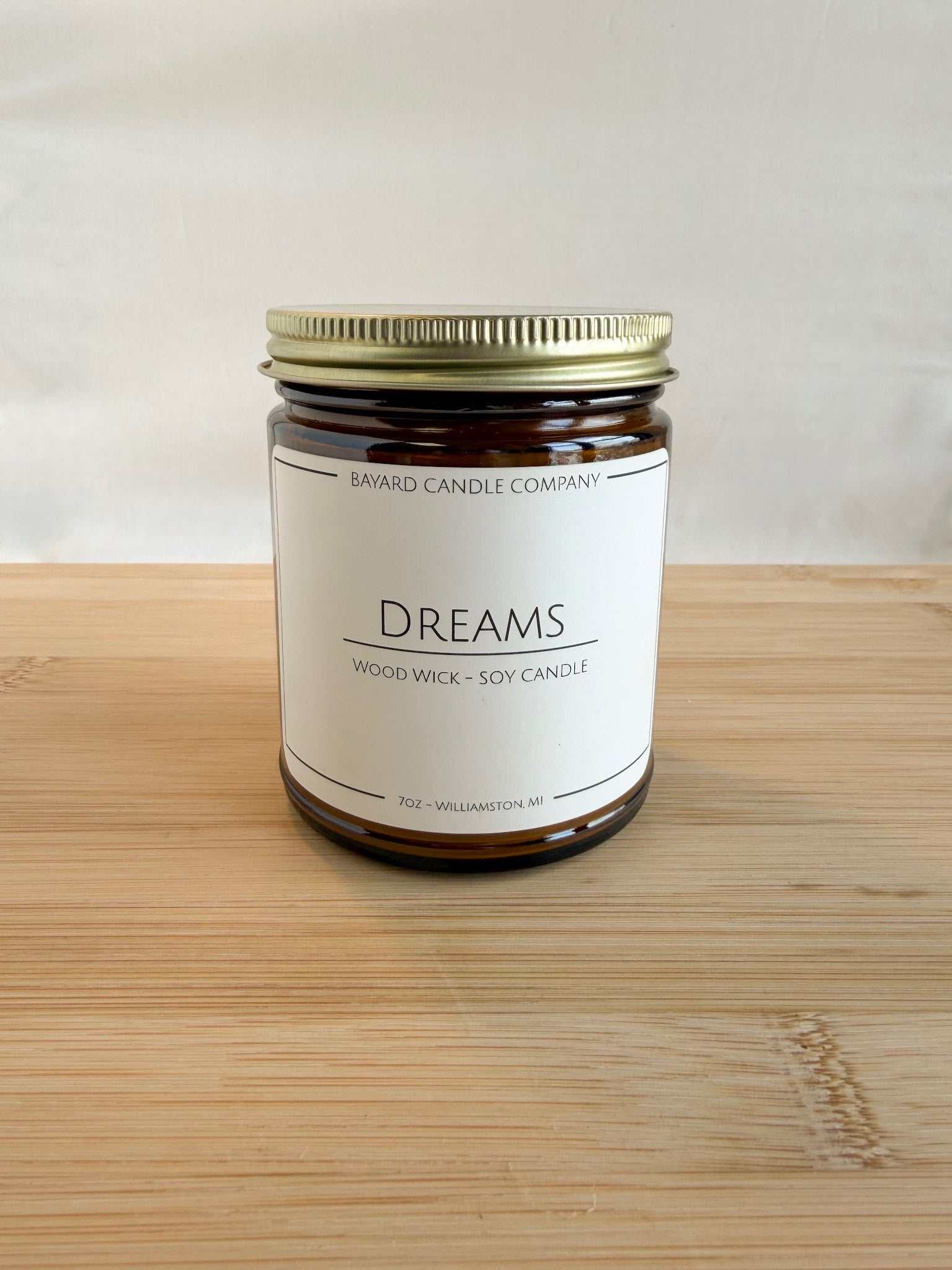 Dreams wood wick soy candle in amber glass jar with gold lid on wood surface, clean minimalist background