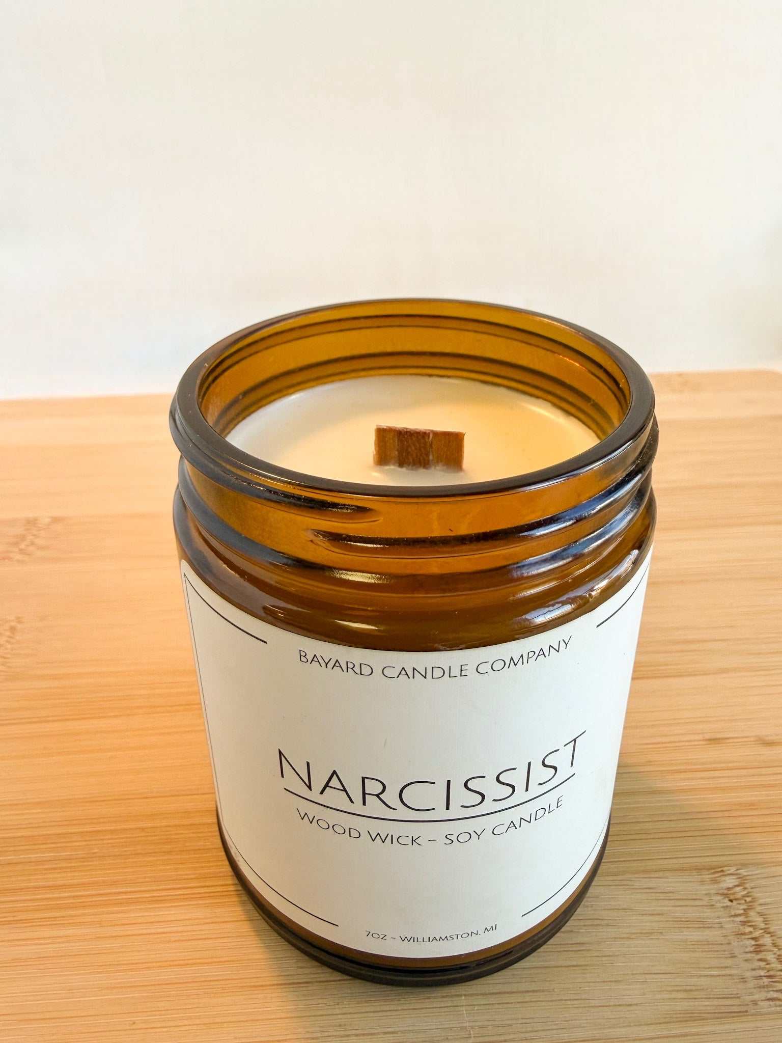 Top view of Narcissist wood wick candle showing smooth soy wax and wooden wick in amber jar