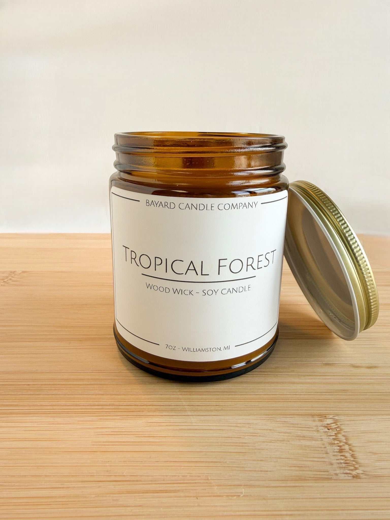 Tropical Forest wood wick soy candle in amber jar with lid off, showing gold lid on side