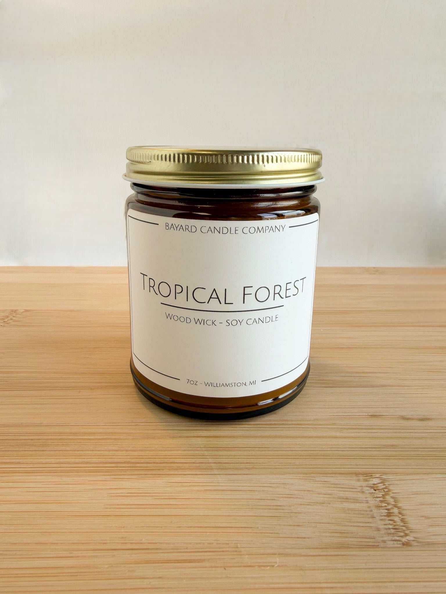Tropical Forest wood wick soy candle in amber glass jar with gold lid on wood surface, clean background