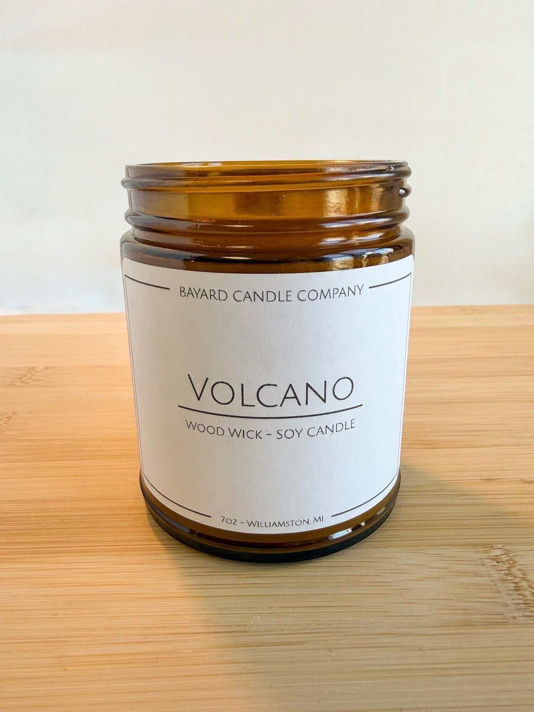 Volcano wood wick soy candle in amber glass jar without lid on wood surface, bright clean aesthetic