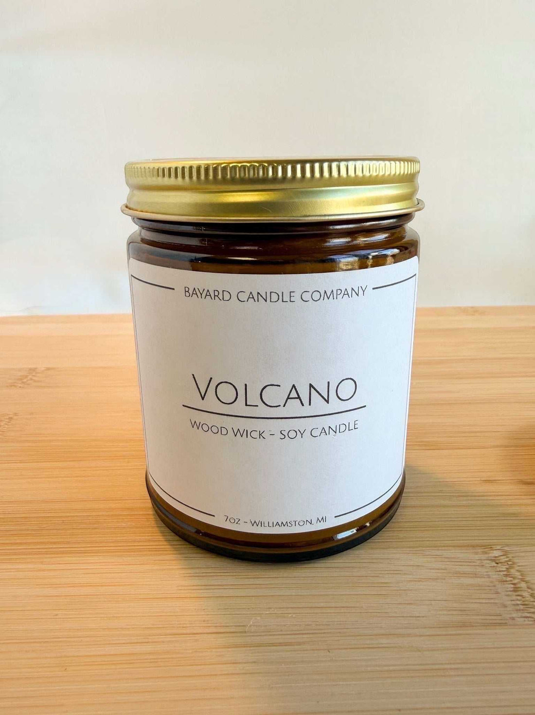 Volcano wood wick soy candle in amber glass jar with gold lid on wood surface, bright clean aesthetic