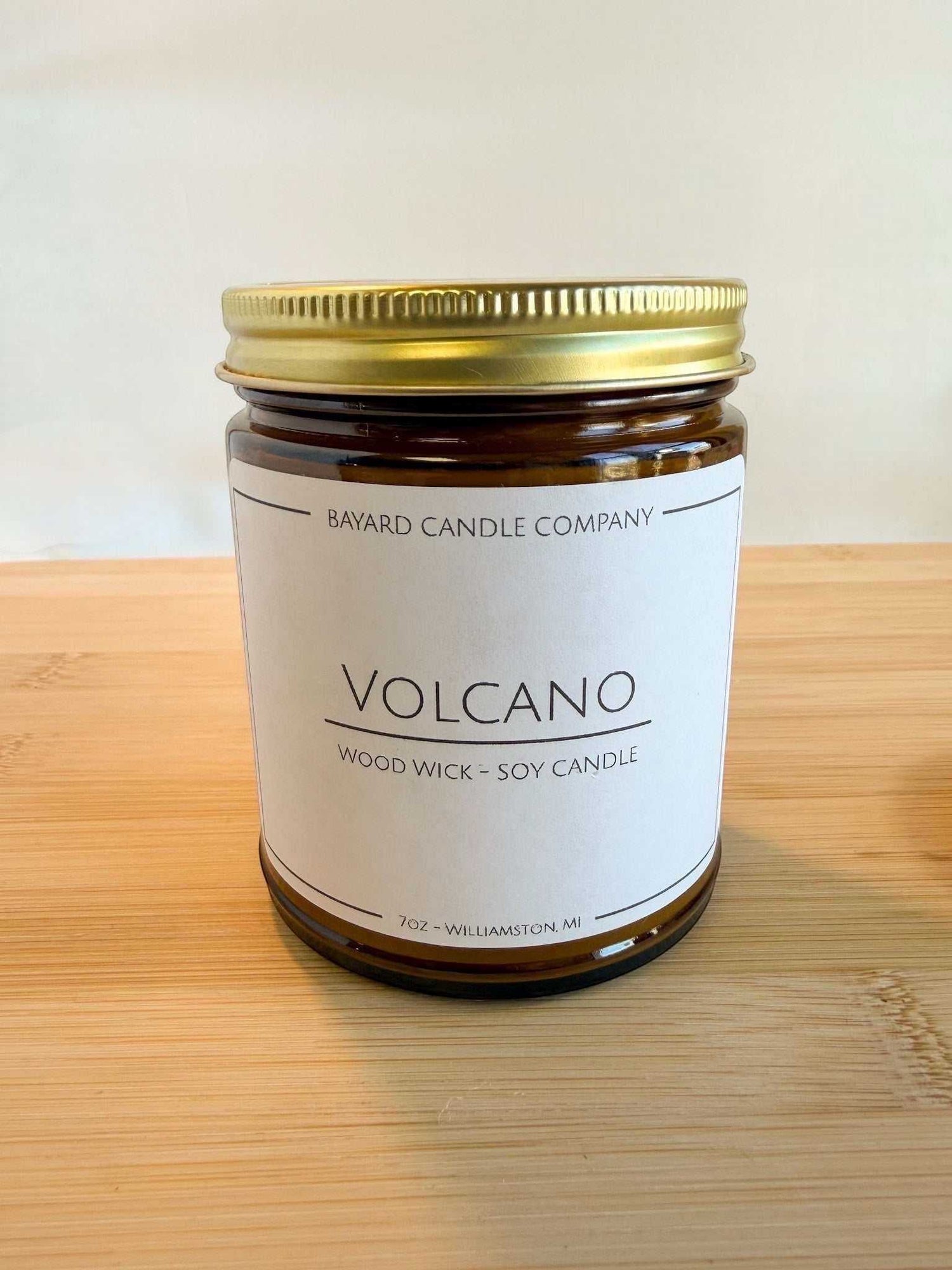 Volcano wood wick soy candle in amber glass jar with gold lid on wood surface, bright clean aesthetic